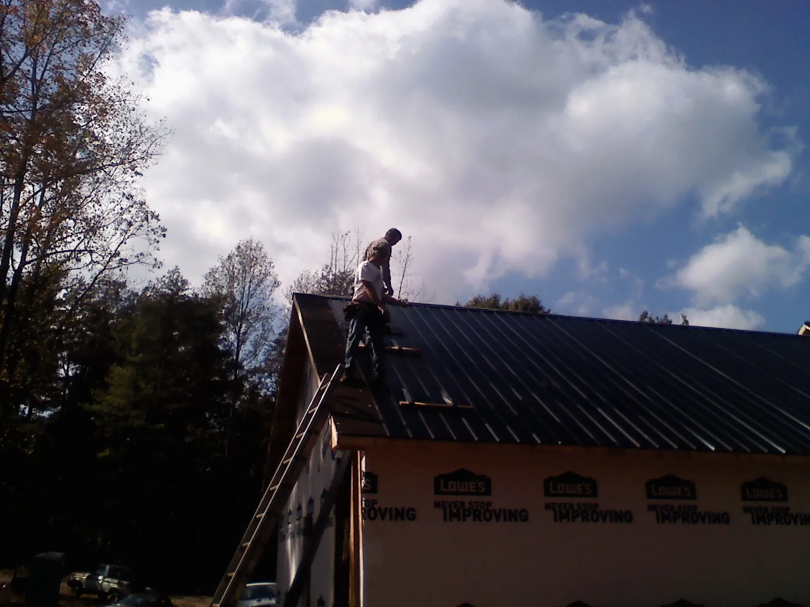 Roofer fastening dark metal panels high against a cloudy sky, from a Roof Inspection job in Independence